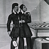 Nineteenth century advertisement for Chang-Eng Bunker’s exhibition tour, circa 1832.  It shows the twins dressed in a specially made Chinese-style suit that reveals their connecting band.  They are standing on a stage beside a bench and table on which is a chess board.  One holds a badminton racquet, while  another badminton racquet and shuttlecock lay on the bench.