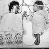 Photograph of the recently separated Rodriguez twins laying side-by-side on a hospital bed.  Clara, on the left, is draped in a hospital blanket; her eyes are open; she is looking at her sister and holding her sister’s IV.  Alta, on the right, is in a hospital gown; her eyes are closed, and her head is in a plastic chamber.  Courtesy The Children’s Hospital of Philadelphia (NLM UI 100961905).