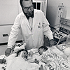 Photograph of Dr. C. Everett Koop standing over a hospital bed in post-operative recovery, where the separated Rodriguez twins lay, side-by-side, draped in hospital blankets.  Clara, on the left, is awake; Alta, on the right, is sleeping.