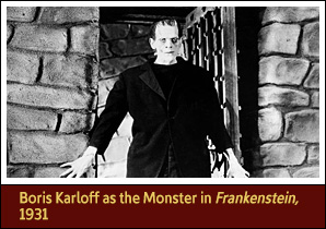 Actor in monster costume, standing in doorway of a room with stone walls and an open, barred door.