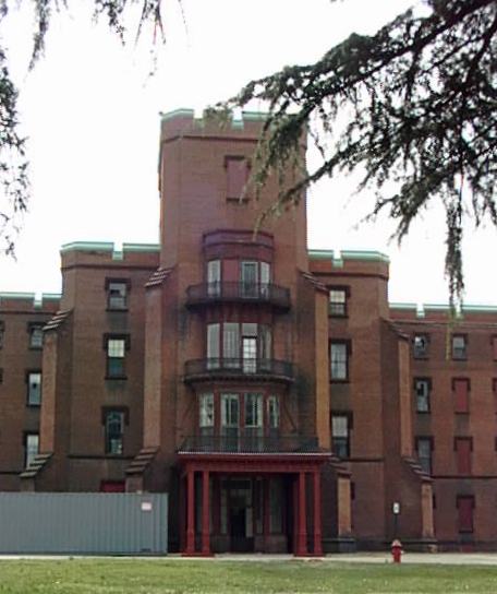A color image of the oldest building at St. Elizabeths Hospital - a multi-story building with 3 balconies on the floors over the entrance and nearby trees.