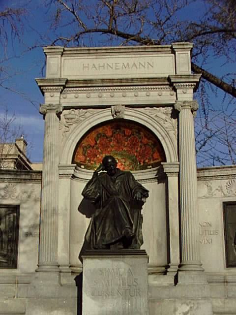 A color image of the Hahnemann Memorial at Scott Circle placed on a large pedestal surrounded by a large archway with two Greek ionic columns.