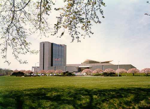 A color photo of the north side view of the National Library of Medicine surrounded by cherry blossom trees and the 10 story Lister Hill center on the left.
