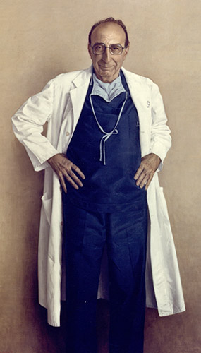 Michael DeBakey standing in blue scrubs and a white lab coat with his hands on his hips.