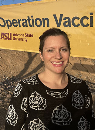 Photograph of a woman with dark hair standing in front of a banner that reads Arizona State University Operation Vaccin....