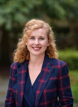 Photograph of a white woman in a navy and red plaid blazer