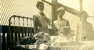 Nurses standing by a patients bed outdoors.