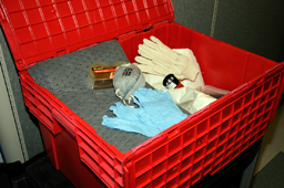 An open red emergency plasic bin showing absorbent matting, tape, gloves, a protective mask, a flash light, and plastic sheeting.