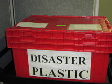 A bright red plastic bin is clearly labeled 'Disaster Plastic.' It is sitting on a movable cart, ready for transport in case of an emergency.