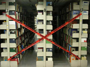 A range of shelving is blocked off at the end with a large 'X' of red tape reading 'Do Not Enter.' The tape is positioned so that the aisles are covered, preventing anyone from walking down them