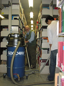 Image depicting wet vac operation.  Attachments are connected to the body of the vacuum in order to allow for more effective vacuuming. Two people are working on the floor of a collection area – one person is using a squeegee to concentrate the water in a specific area, where the person with the vacuum is collecting it.