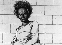 A scowling woman with her arms held in a gown sitting with her feet drawn up on a bench, and leaning against a tiled wall.