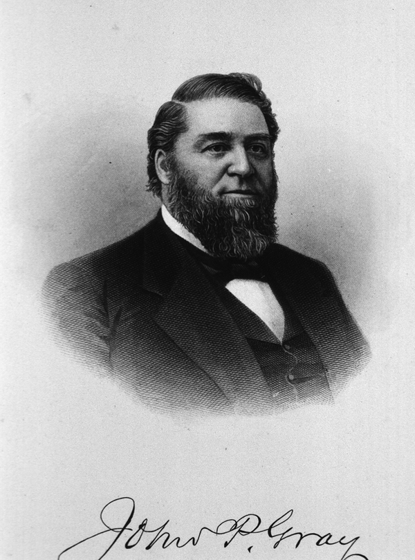 A formal photograph of a full bearded man in a suit with a printed autograph at the bottom.