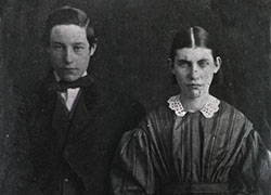 A young man on the left and a young woman on the right in formal, late 19th-century attire looking directly into the camera.