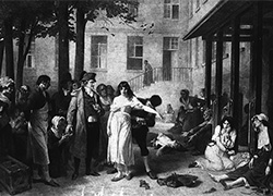 A man stands in the courtyard as a woman patient is freed from her chains; other women patients are chained to wooden posts attached to a building.