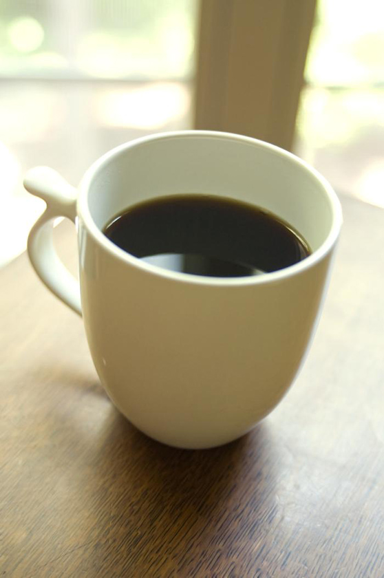 A cup of coffee in a white mug on a wooden table near a window.