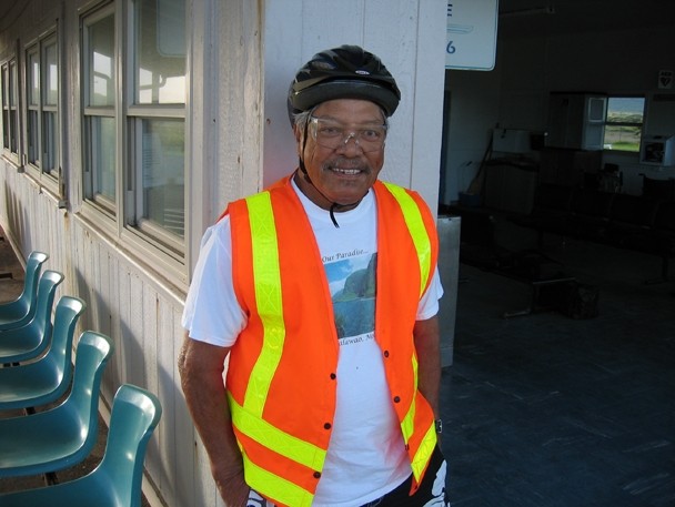 Color image of a man wearing a helmet, clear safety glasses, and an orange and yellow safety vest.
