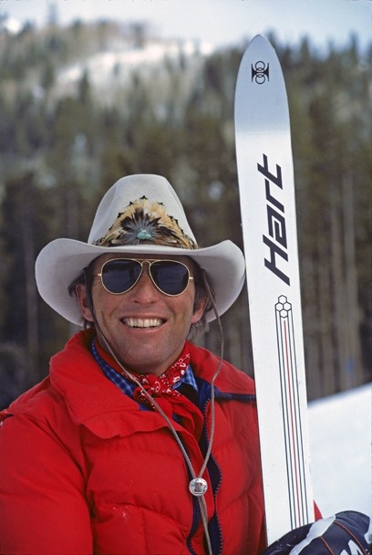 Black and white photograph of Billy Kidd wearing sunglasses and a hat while holding his skis.