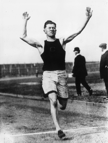 Black and white photograph of Jim Thorpe running with his hands in the air.