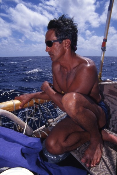 Color image of Nainoa Thompson wearing sunglasses, sitting on a boat, and looking out into the water. Color image of Nainoa Thompson wearing sunglasses, sitting on a boat, and looking out into the water.