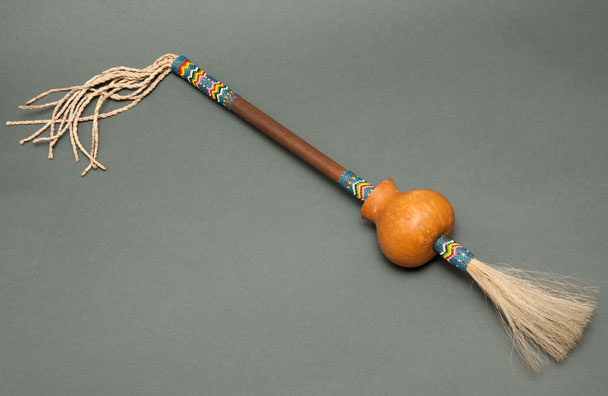 Color image of a long, handmade rattle with intricate designs on its shaft.