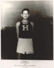 Black and white photograph of Billy Mills standing with his hands behind his back while wearing running attire.