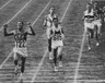 Black and white photograph of Billy Mills throwing his hands in the air as he finishes first in an Olympic race.