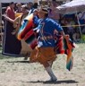 Color photograph of a Native American female dancing while wearing a blue top and holding a multi-colored blanket.