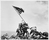 Black and white photograph of four soldiers working together to hoist up an American flag attached to a pole.