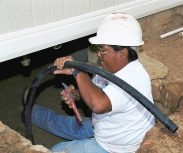 Color photograph of a man in a hardhat connecting a water line on the Navajo Reservation in New Mexico.