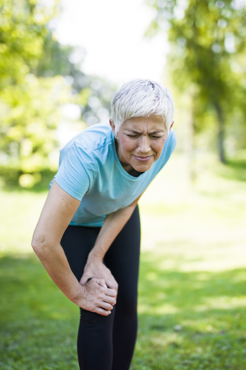 Senior sportswoman with knee pain standing in park stock photo