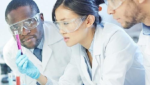 Three scientists in goggle looking at a test tube