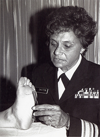 Dr. Marilyn Hughes Gaston, an African American female in military uniform inspecting a bare foot.